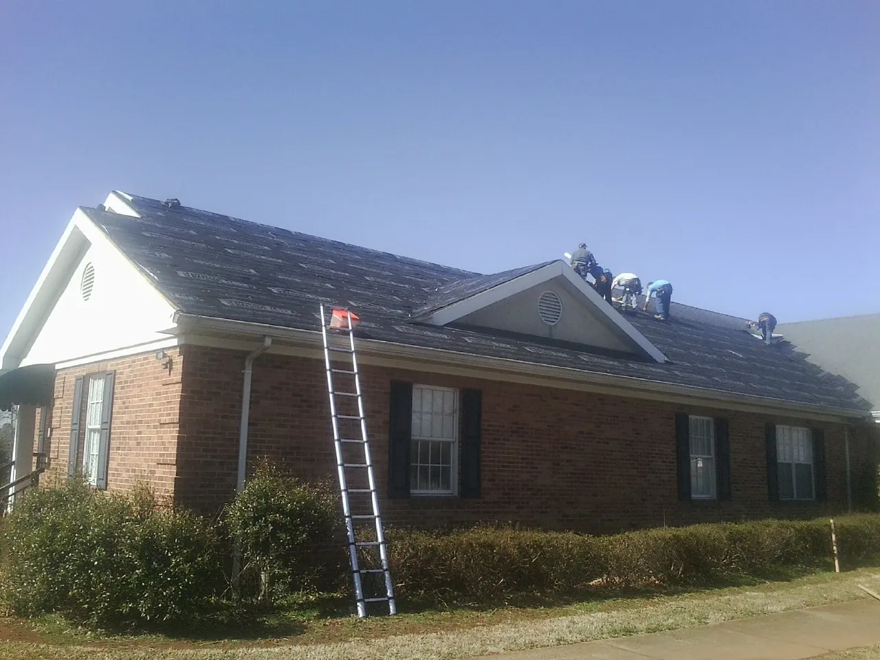 Crew tearing shingles off a brick ranch roof with a ladder set — Metal Roof Repair work by our crew in Bailey