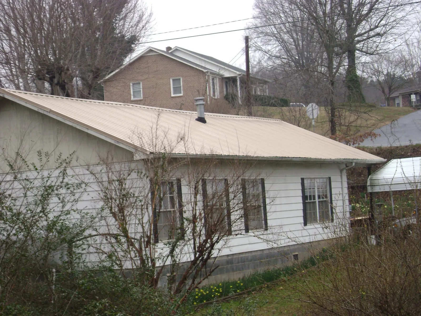 Tan metal roof on a white sided house set into a hillside — Commercial Roofing by Roofing Brothers in Bailey